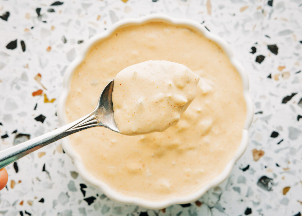Dipping a spoon into creamy, dye-free copycat Big Mac sauce made with real-food ingredients for a healthier simple swap.