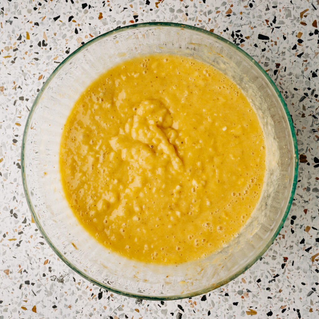 Mixing raw honey, melted butter, and eggs into the mashed banana base for a honey sweetened ingredient batter.