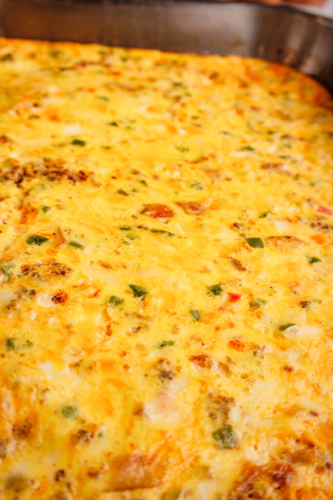 Close-up of a baked breakfast casserole showing melted cheese, savory sausage, and colorful bell peppers in a fluffy egg base.