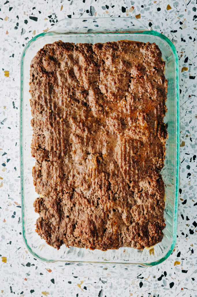Baked ground beef sheet for sliders in a 9x13 pan with rendered juices drained off.