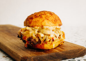 A single Bourbon Street slider with grass-fed beef, white cheddar, and honey-bourbon glaze on a white plate.