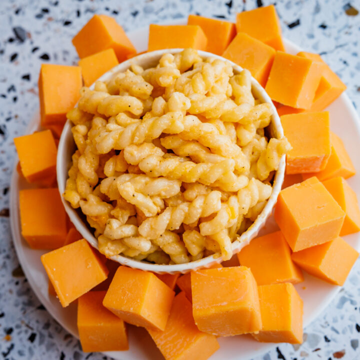 A white bowl of creamy mac and cheese served with stacks of real cheddar cheese cubes, made with no processed ingredients.