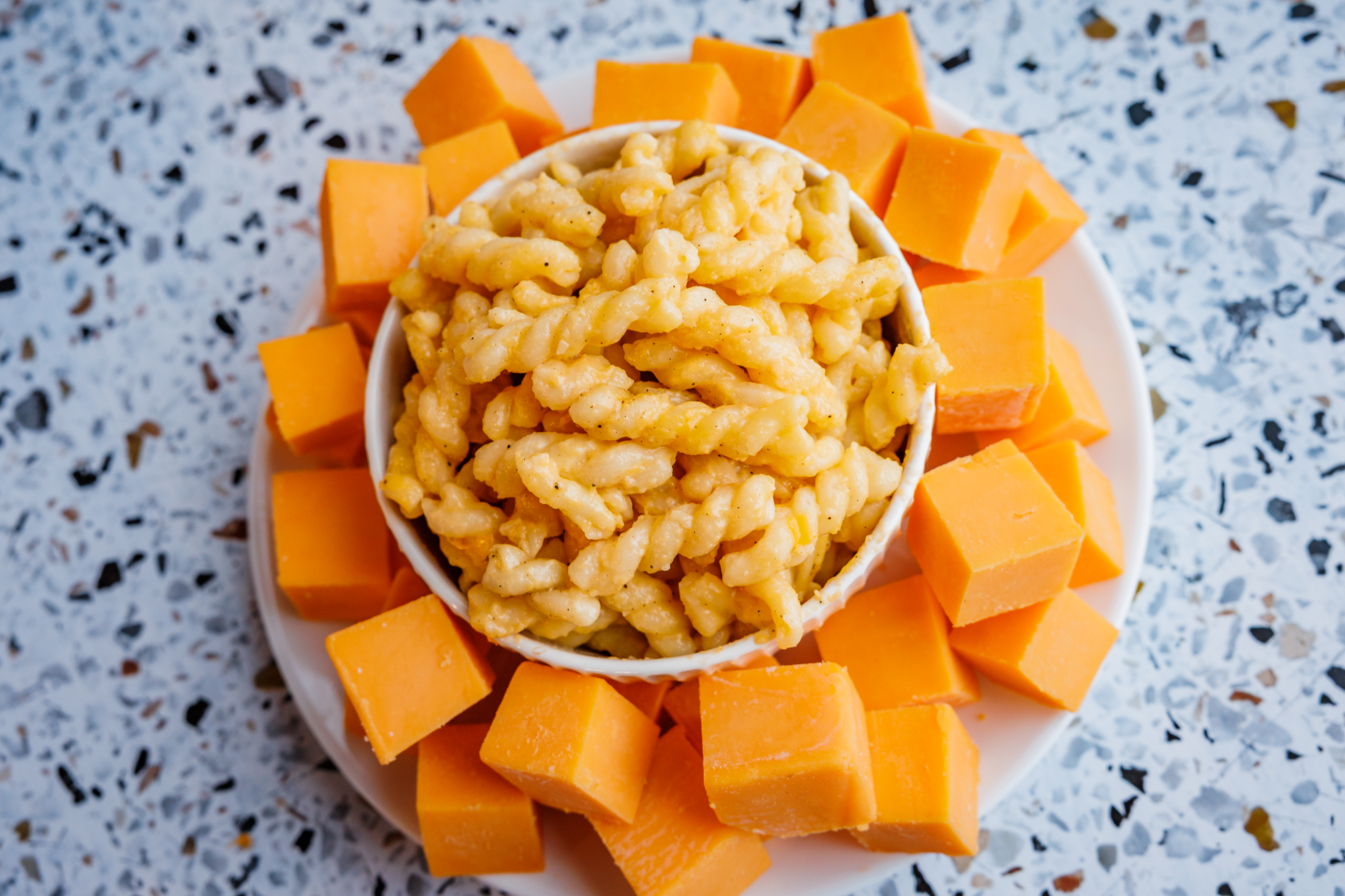 A white bowl of creamy mac and cheese served with stacks of real cheddar cheese cubes, made with no processed ingredients.