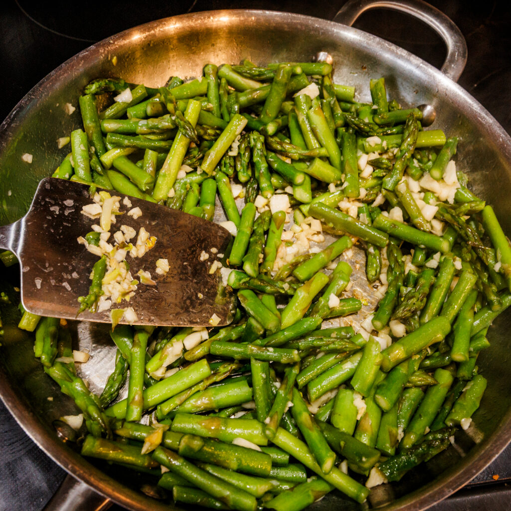 Sautéing fresh asparagus and minced garlic in a stainless steel skillet for a healthy lemon chicken stir fry.