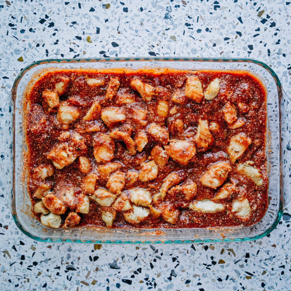 chicken breast stirred into pasta sauce and parmesan cheese in a 9x13