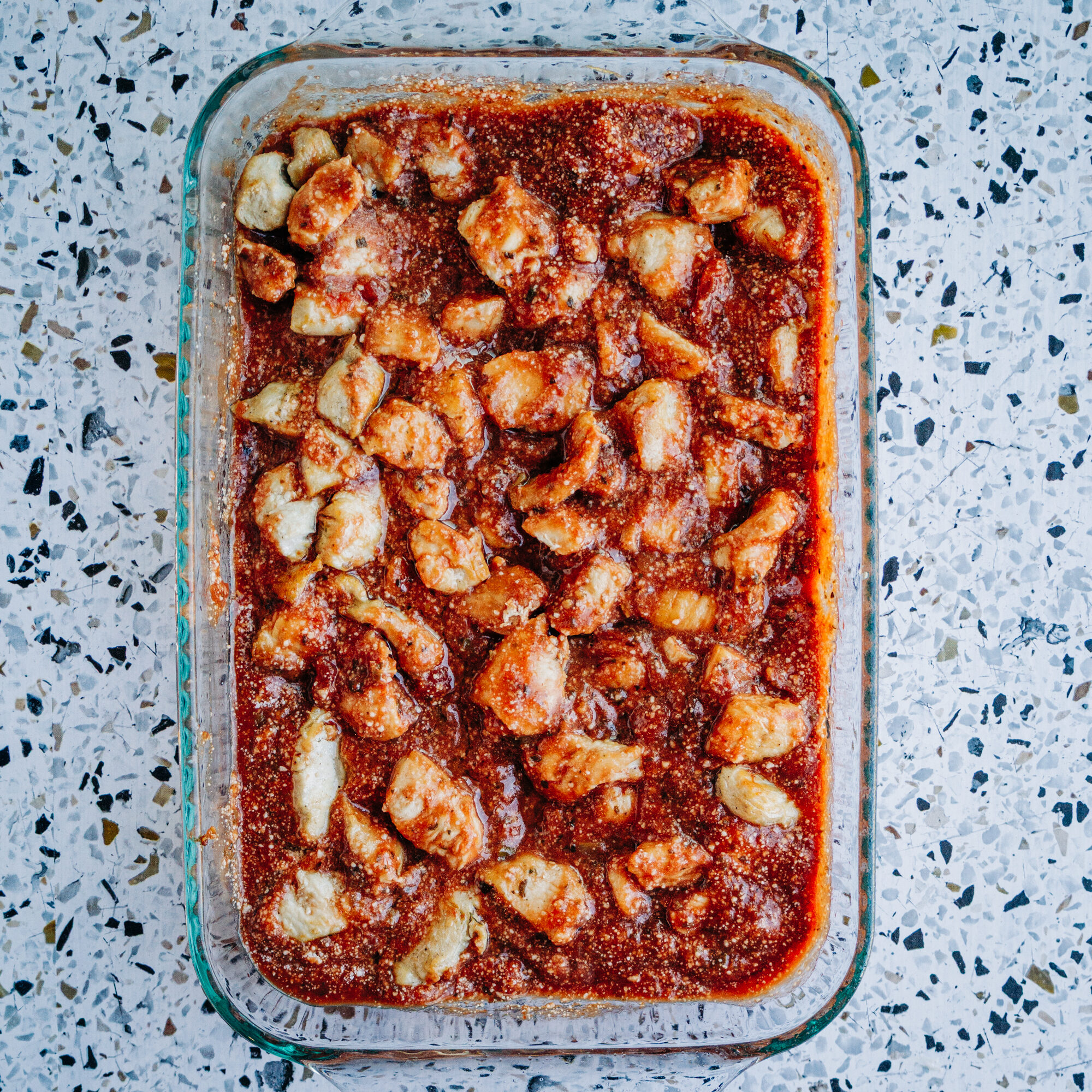 chicken breast stirred into pasta sauce and parmesan cheese in a 9x13