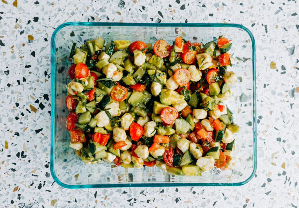 a summer cookout ready fresh salad made of cucumber. tomatoes, avocados, and basil with mozzarella pearls