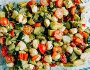 a fresh salad made of cucumber. tomatoes, avocados, and basil with mozzarella pearls