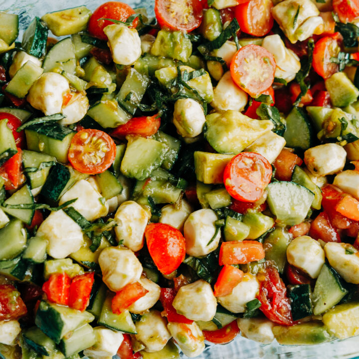 a fresh salad made of cucumber. tomatoes, avocados, and basil with mozzarella pearls