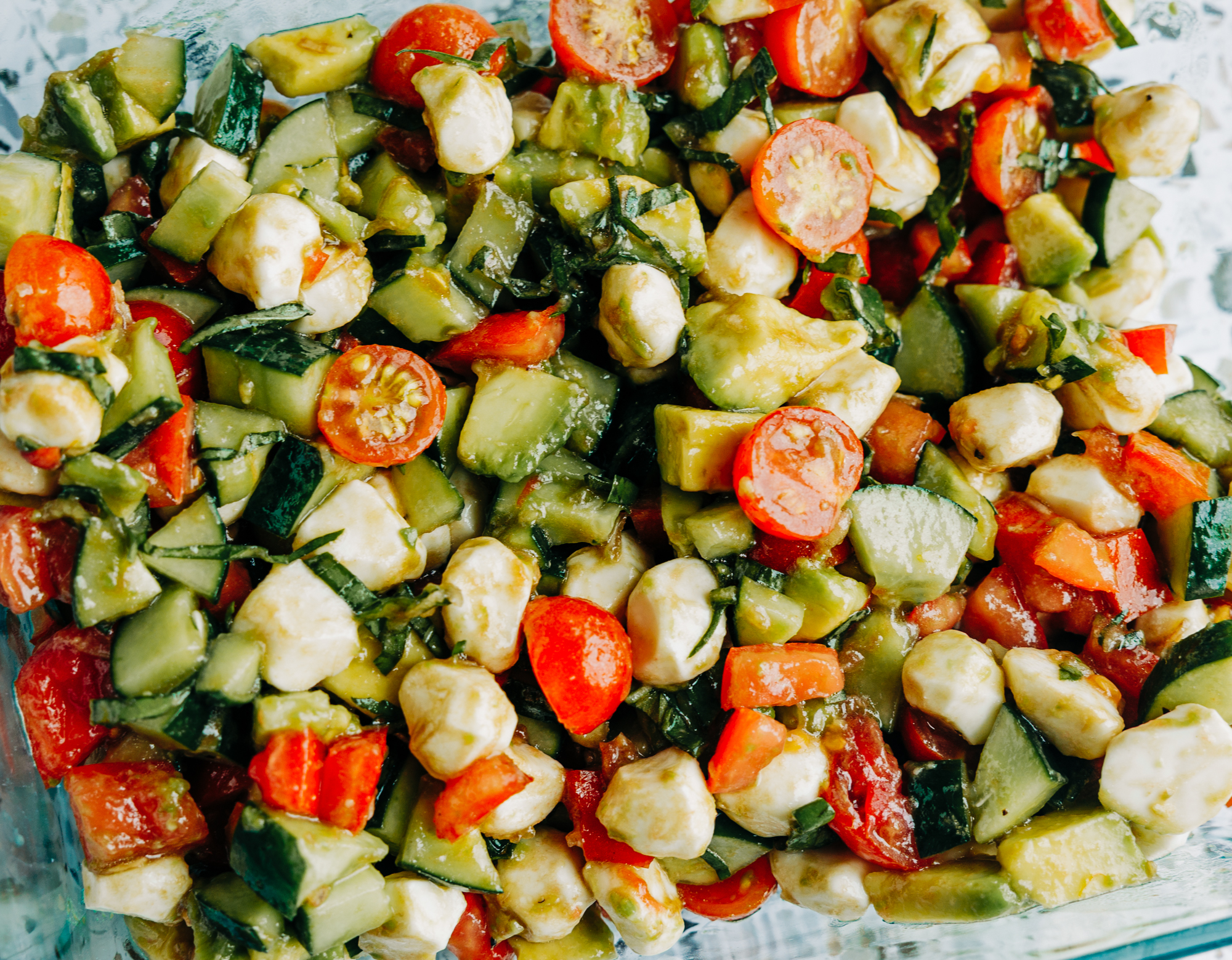 a fresh salad made of cucumber. tomatoes, avocados, and basil with mozzarella pearls