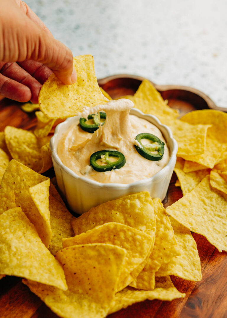 a tortilla chip dipped into a jalapeño popper dip that is garnished with jalapeño slices.